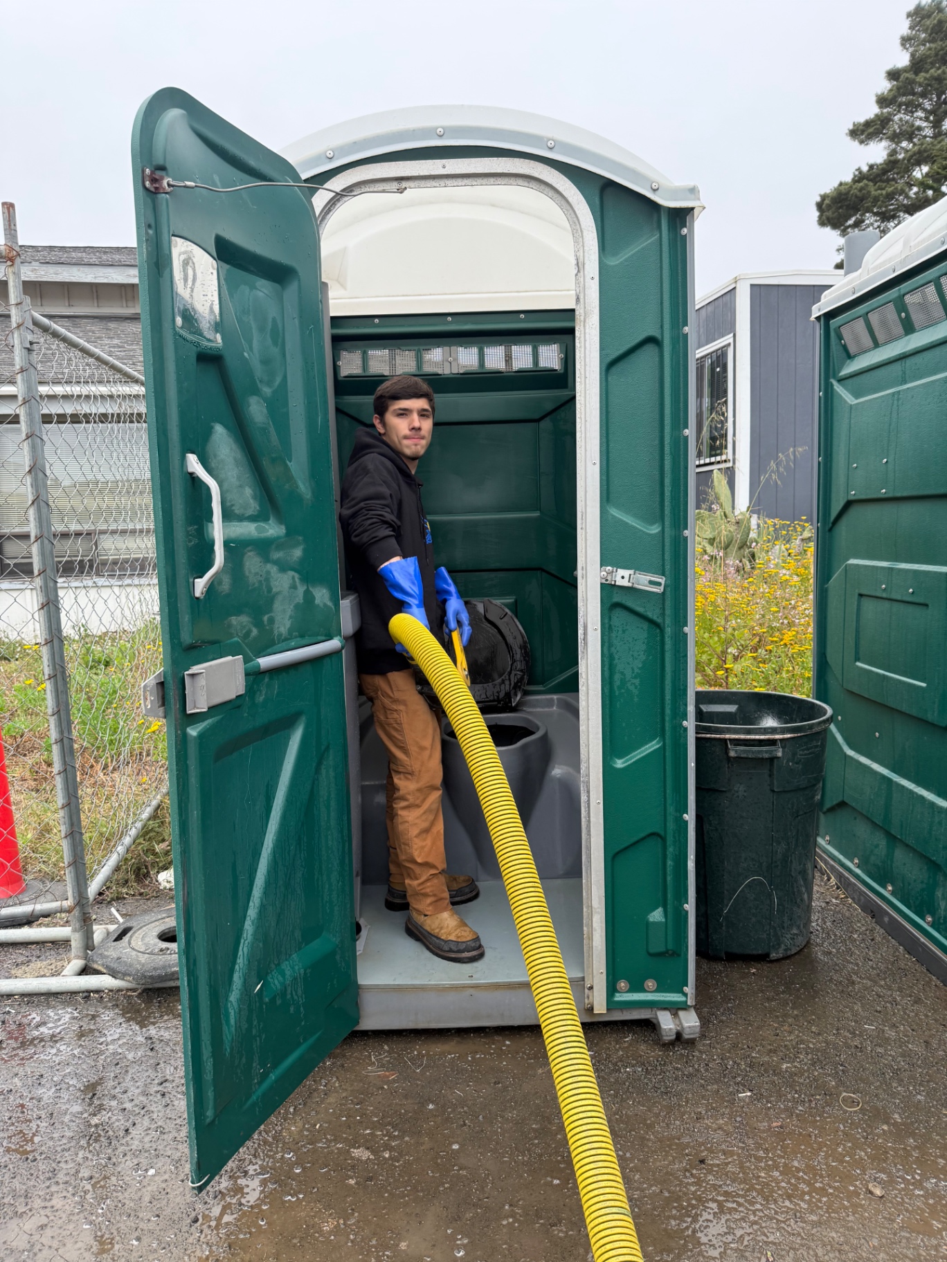 CNA Coastal Portables technician servicing a portable restroom unit with a yellow suction hose
