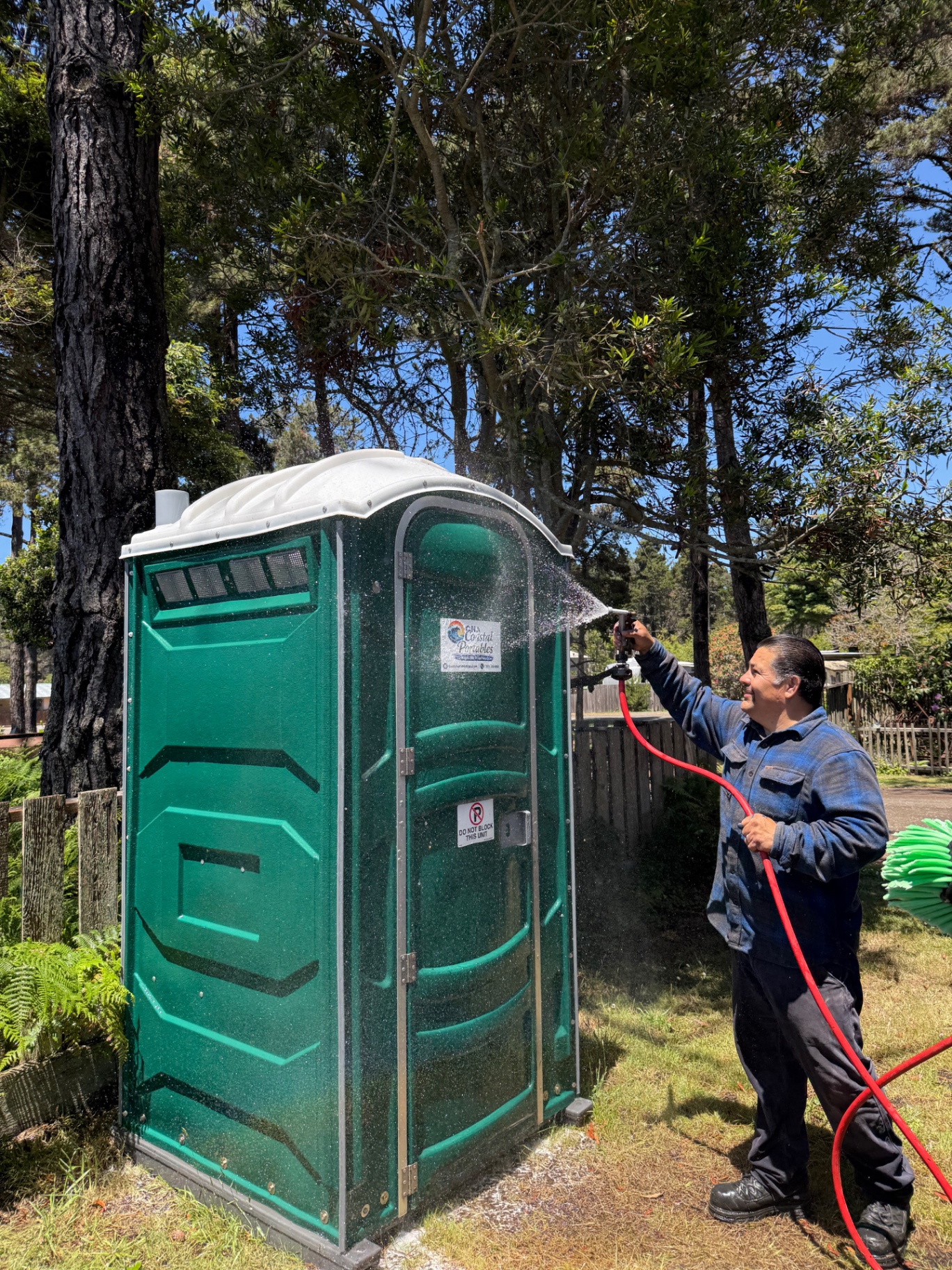 CNA Coastal Portables technician cleaning a well-maintained green portable restroom unit on a sunny coastal property
